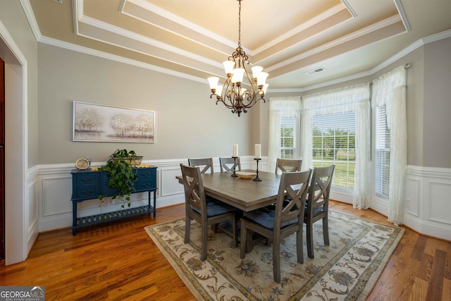 dining area with a raised ceiling, crown molding, hardwood / wood-style floors, and a chandelier