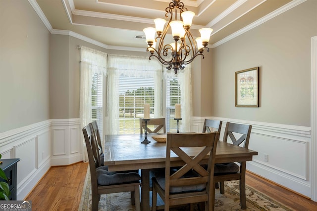 dining room with ornamental molding, light hardwood / wood-style floors, a tray ceiling, and a chandelier