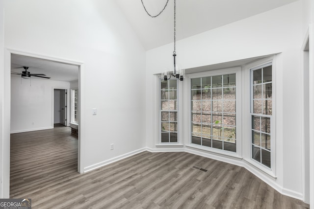 unfurnished dining area with hardwood / wood-style floors, ceiling fan with notable chandelier, and high vaulted ceiling