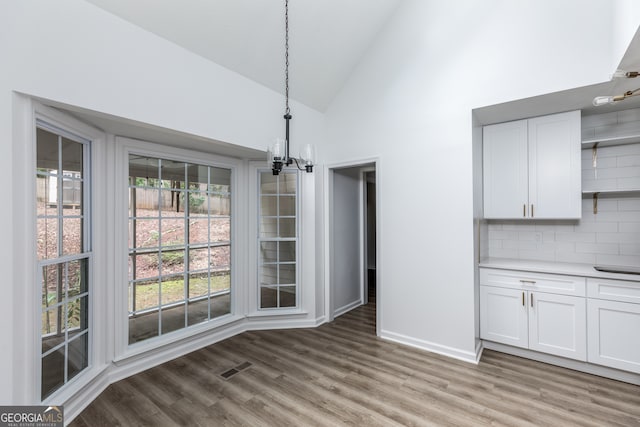 unfurnished dining area with high vaulted ceiling, a chandelier, and light hardwood / wood-style flooring