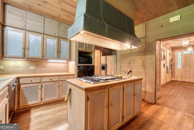 kitchen featuring wood walls, a center island, light hardwood / wood-style floors, and black appliances