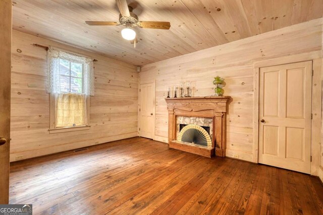 unfurnished living room featuring wood walls, a fireplace, wood ceiling, ceiling fan, and hardwood / wood-style flooring