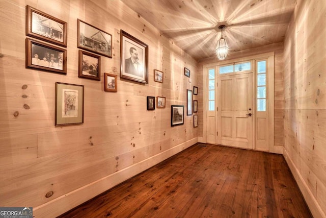 entrance foyer with dark wood-style floors, wooden walls, and baseboards