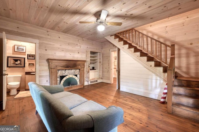 living room with wood walls, wood ceiling, ceiling fan, hardwood / wood-style flooring, and a premium fireplace