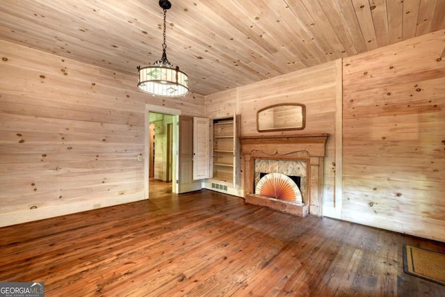 unfurnished living room with a fireplace with raised hearth, dark wood-style flooring, wood walls, wood ceiling, and visible vents