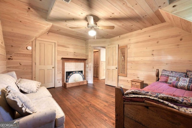 bedroom with ceiling fan, wood walls, a tiled fireplace, and dark wood-type flooring