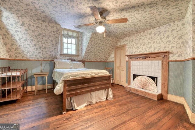 bedroom with a tiled fireplace, ceiling fan, and wood-type flooring