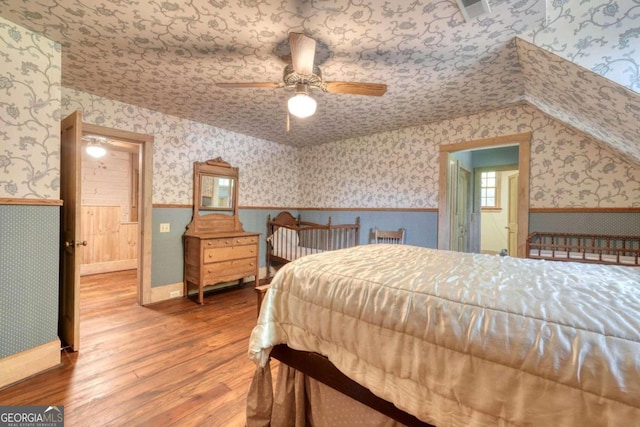 bedroom with wallpapered walls, a wainscoted wall, and wood finished floors