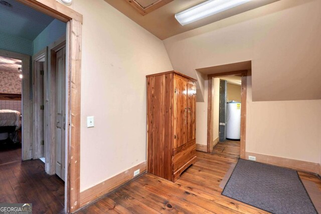 corridor with vaulted ceiling, gas water heater, and dark wood-type flooring