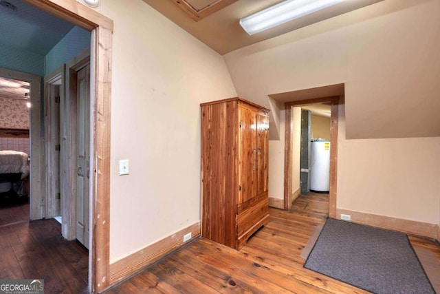 corridor with baseboards, water heater, vaulted ceiling, and hardwood / wood-style floors