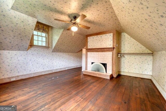 additional living space featuring a textured ceiling, a tiled fireplace, hardwood / wood-style floors, and lofted ceiling