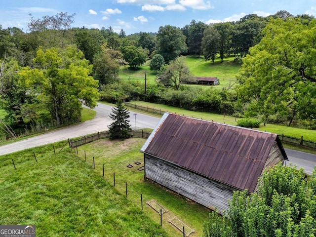 surrounding community featuring a rural view, fence, a lawn, and an outbuilding