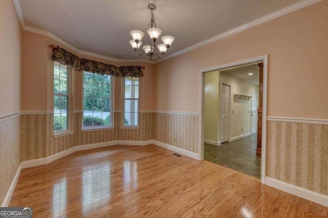 unfurnished room featuring crown molding, wood-type flooring, and an inviting chandelier