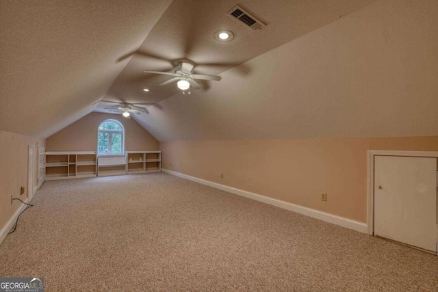 additional living space with light colored carpet, vaulted ceiling, a textured ceiling, and ceiling fan