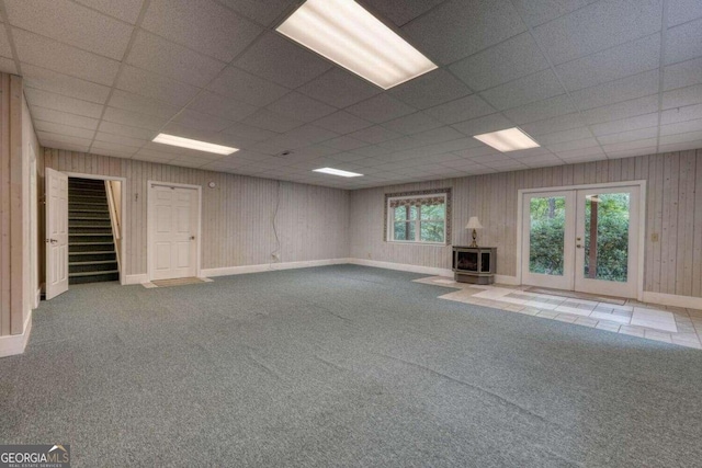 interior space with wood walls, a drop ceiling, french doors, and carpet flooring