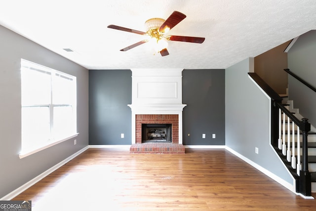 unfurnished living room with a fireplace, ceiling fan, a textured ceiling, and wood-type flooring