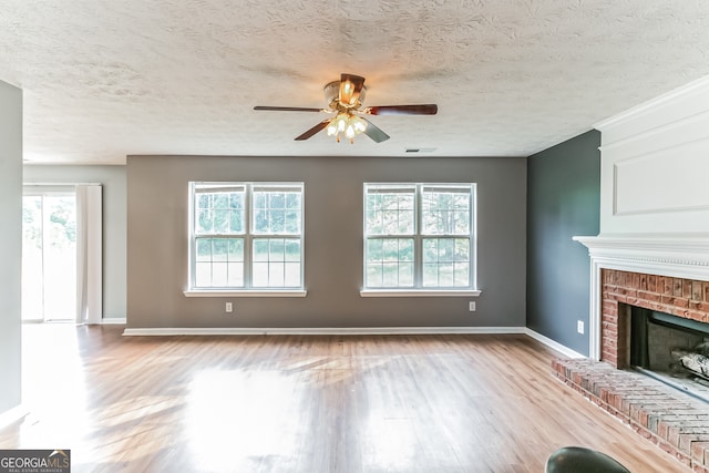 unfurnished living room featuring a textured ceiling, ceiling fan, light wood-type flooring, and a brick fireplace