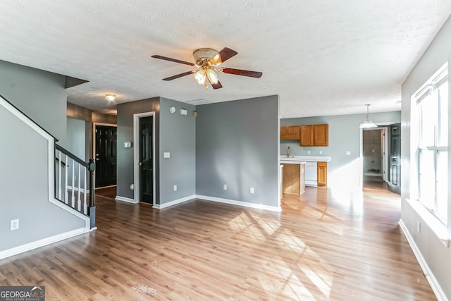 unfurnished living room featuring sink, light hardwood / wood-style flooring, ceiling fan, and a textured ceiling