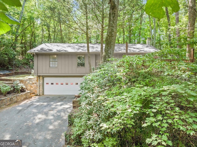 view of front facade featuring a shingled roof, aphalt driveway, an attached garage, and a chimney