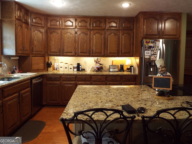 kitchen with sink, light stone countertops, decorative backsplash, appliances with stainless steel finishes, and hardwood / wood-style flooring