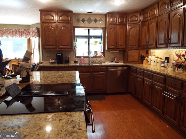 kitchen with light stone countertops, dark hardwood / wood-style flooring, dishwasher, sink, and decorative backsplash