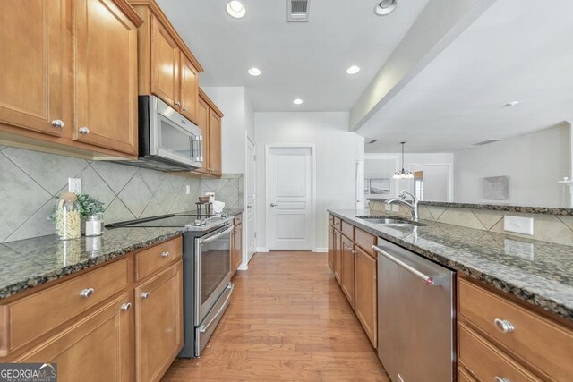 kitchen with a kitchen island with sink, light hardwood / wood-style flooring, stainless steel appliances, hanging light fixtures, and a breakfast bar area