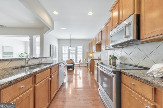 kitchen with appliances with stainless steel finishes, sink, decorative backsplash, dark stone countertops, and light wood-type flooring