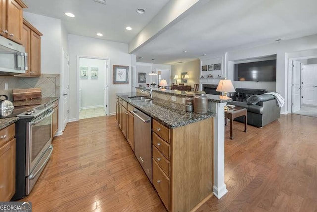 kitchen featuring a kitchen island with sink, tasteful backsplash, light hardwood / wood-style floors, stainless steel appliances, and dark stone counters