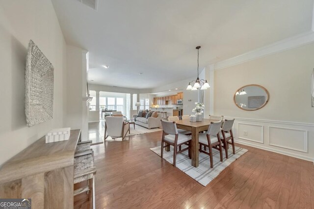 dining space with decorative columns, hardwood / wood-style flooring, a chandelier, and crown molding