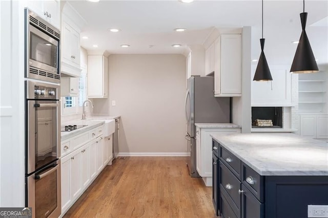 kitchen featuring hanging light fixtures, light stone counters, light hardwood / wood-style floors, white cabinetry, and stainless steel appliances