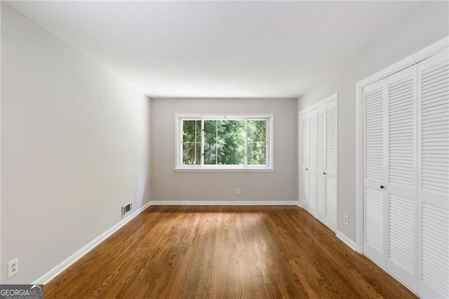 unfurnished bedroom with two closets and hardwood / wood-style flooring