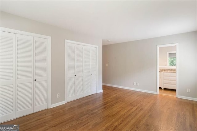 unfurnished bedroom with multiple closets, hardwood / wood-style flooring, and connected bathroom