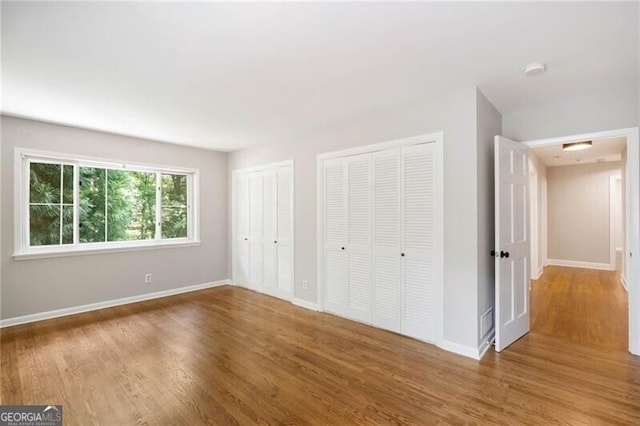 unfurnished bedroom featuring hardwood / wood-style floors and multiple closets