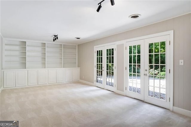 carpeted empty room featuring rail lighting, french doors, and built in features