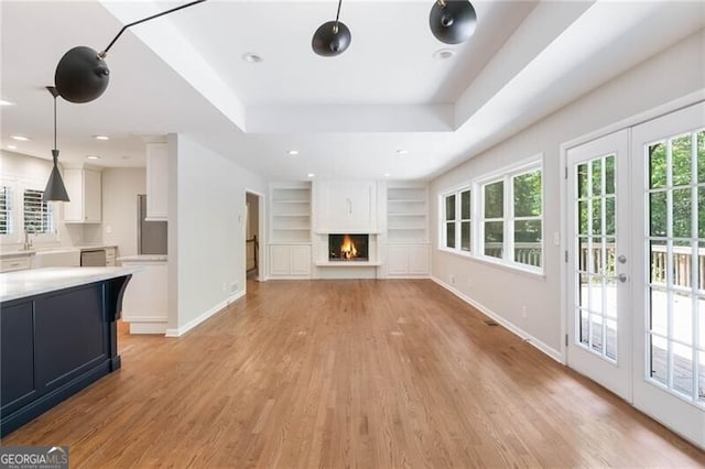 unfurnished living room featuring light hardwood / wood-style floors, a raised ceiling, built in shelves, and french doors