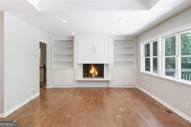 unfurnished living room featuring built in features, a fireplace, and light hardwood / wood-style flooring