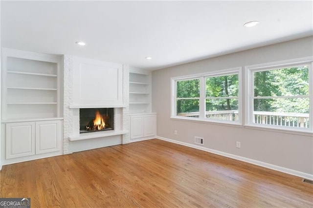 unfurnished living room with a fireplace, light hardwood / wood-style flooring, and built in shelves