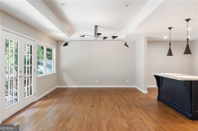 unfurnished living room featuring light hardwood / wood-style floors, a raised ceiling, a notable chandelier, and french doors