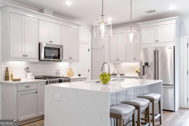 kitchen featuring stainless steel appliances, white cabinetry, tasteful backsplash, pendant lighting, and a kitchen island with sink