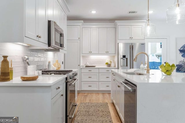 kitchen with stainless steel appliances, white cabinetry, a kitchen island with sink, and pendant lighting