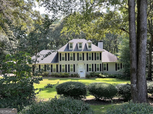 view of front of property featuring roof with shingles, a chimney, and a front yard