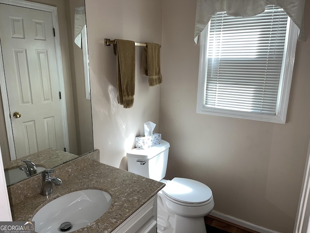 half bathroom featuring baseboards, vanity, and toilet