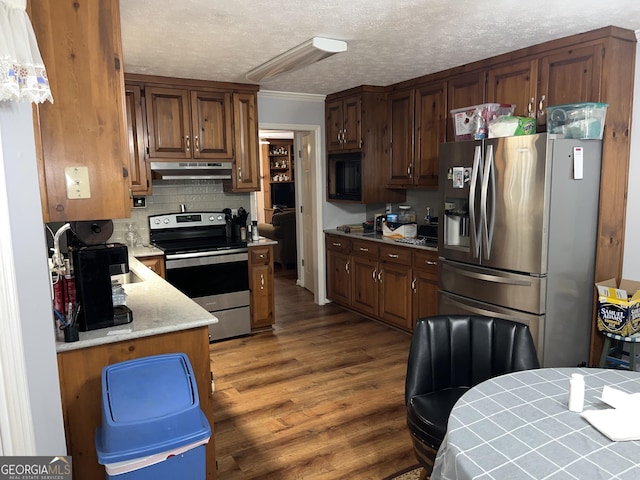 kitchen with decorative backsplash, dark wood-style floors, appliances with stainless steel finishes, light countertops, and under cabinet range hood