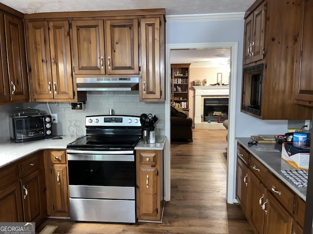 kitchen featuring crown molding, a fireplace with raised hearth, light countertops, under cabinet range hood, and stainless steel electric range