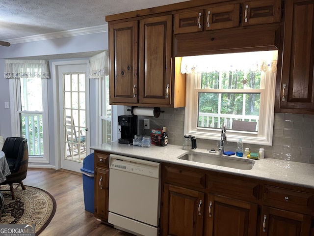 kitchen featuring white dishwasher, wood finished floors, a sink, light countertops, and crown molding