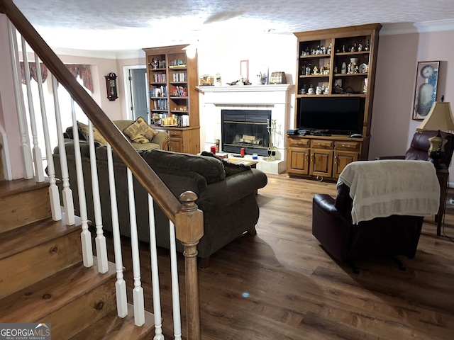 living room featuring ornamental molding, a glass covered fireplace, a textured ceiling, wood finished floors, and stairs