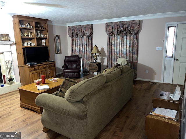 living room with a textured ceiling, ornamental molding, wood finished floors, and baseboards