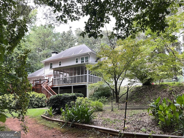 back of property featuring a chimney, a sunroom, stairway, and a deck