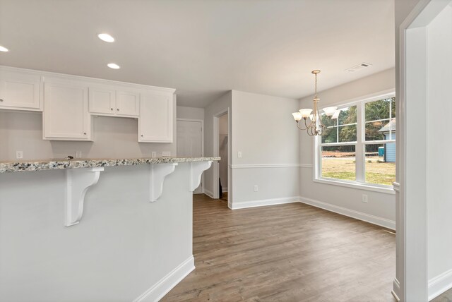 kitchen with a kitchen bar, light stone countertops, dark hardwood / wood-style flooring, an inviting chandelier, and white cabinets