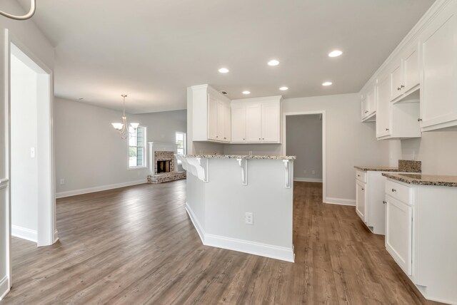 kitchen with a kitchen bar, a brick fireplace, dark stone counters, white cabinets, and hardwood / wood-style floors